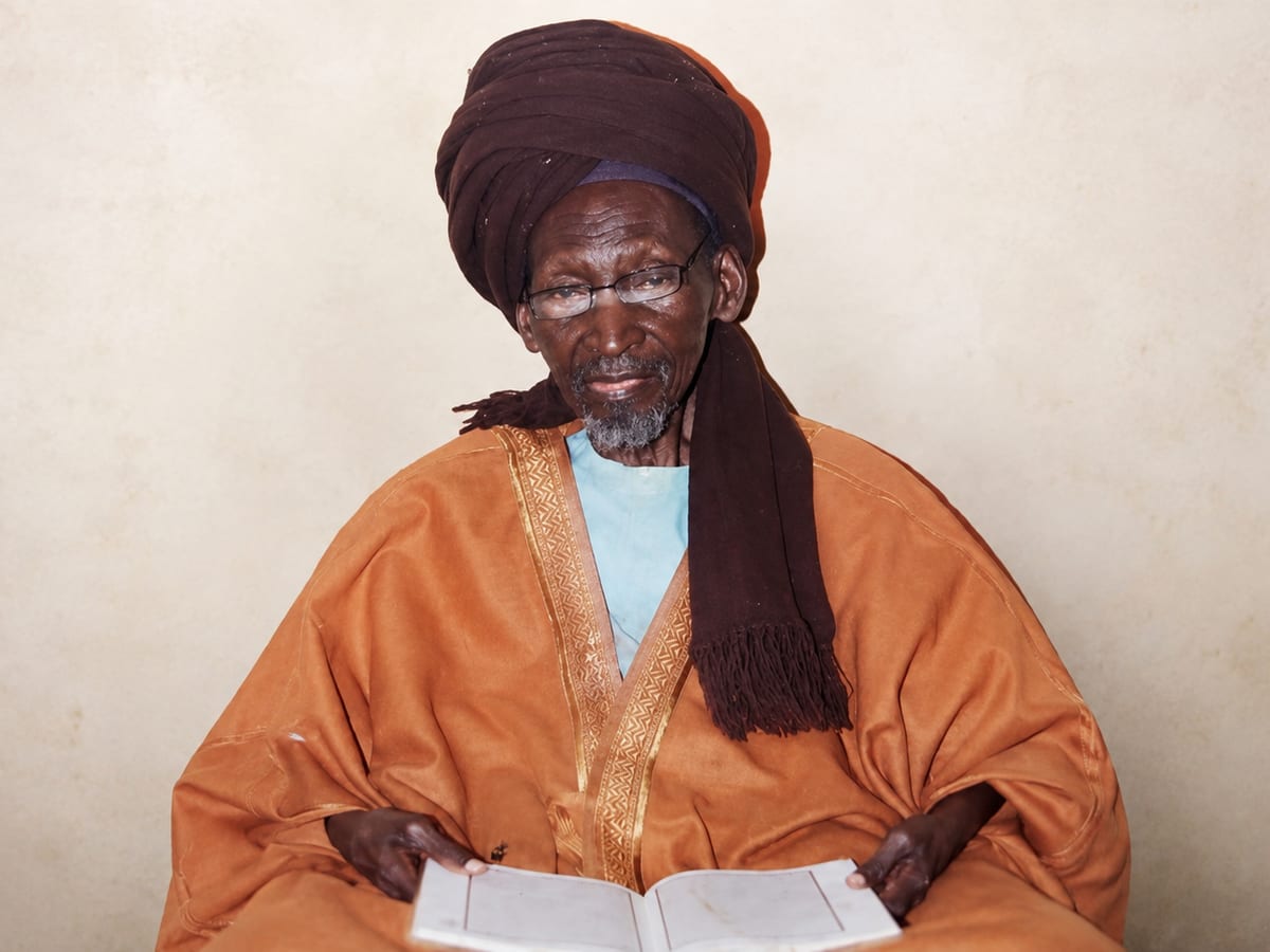 Le Professeur Balseny, en boubou et turban, lisant son livre de consultation